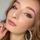 A woman wearing large earrings and pink lips, proudly displaying her DIY lash extensions in a bright setting.